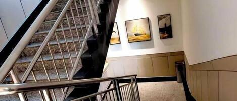 A staircase with metal railings, a carpeted floor, and two framed pictures on the wall.