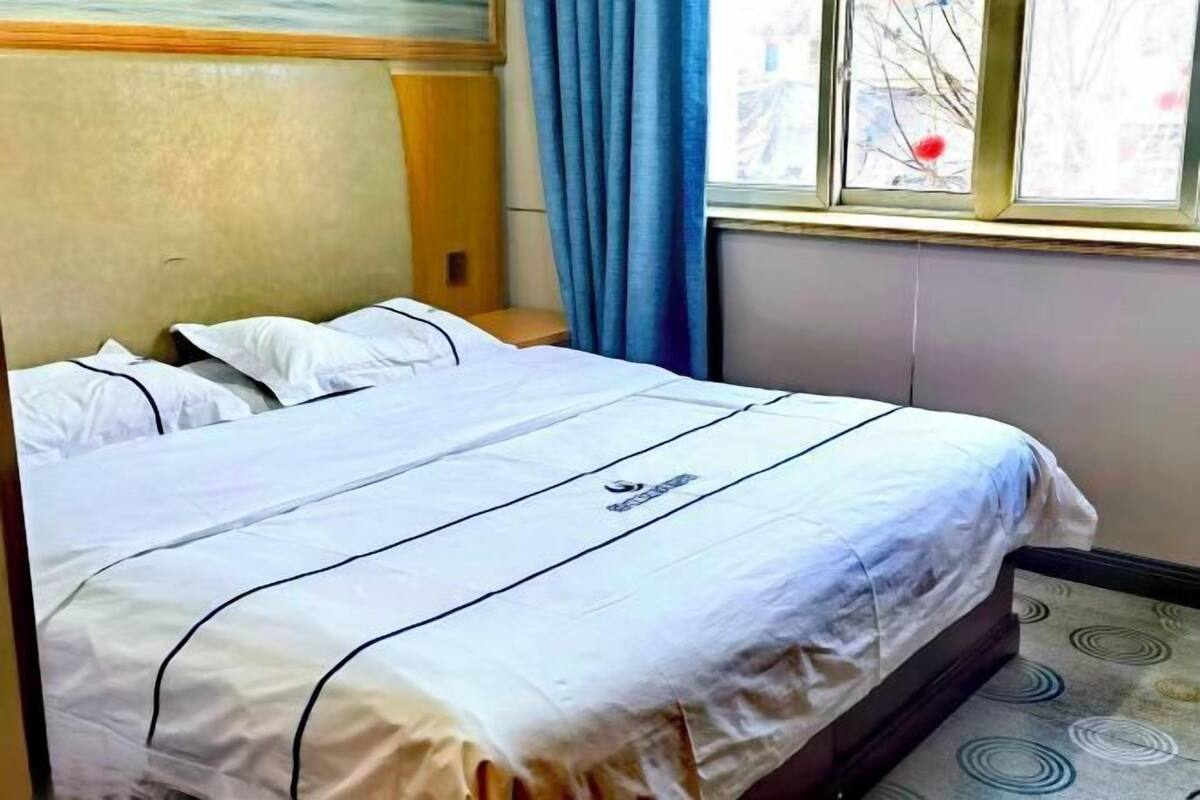 A hotel room with a bed, a window with curtains, and a view of the outside.