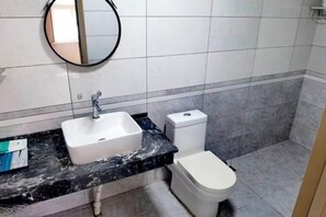 A bathroom with a white sink, a toilet, and a round mirror on the wall. - Wuqiyanda Hotel (Wuqi)