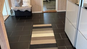 A modern interior with a dark tiled floor, a striped rug, a sofa with pillows, wooden paneling, a map on the wall, and a door leading to a bathroom. - Lovely and well equipped home with outdoor BBQ, ready for hiking in Seljestad. (Ullensvang)