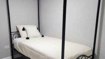 A four-poster bed with a white mattress and pillows, set on a wooden floor in a room with white walls and a ceiling light.