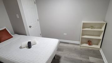 A bedroom with a bed, a white door, a white shelf unit, and a grey wall.