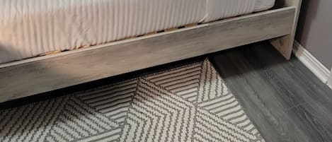 A bed with a headboard, a bedside table, and a patterned rug.