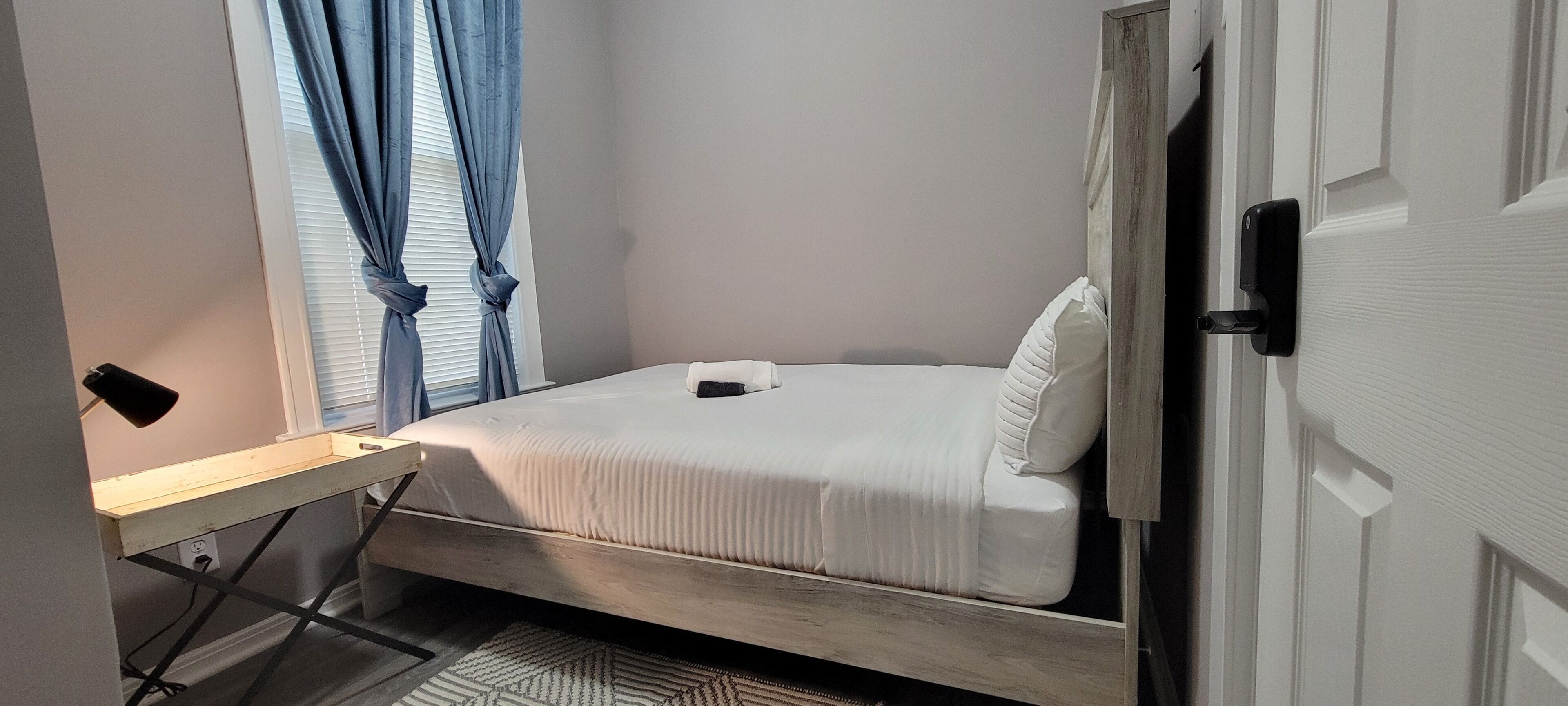 Une chambre à coucher de taille modeste, comprenant un lit, un petit bureau et une fenêtre avec des rideaux.