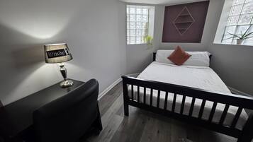 Un dormitorio con cama, escritorio y lámpara. Hay ventanas con cortinas y un adorno decorativo sobre la cama.