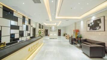 A hotel reception area with a reception desk, seating area, and a hallway leading to the rooms.