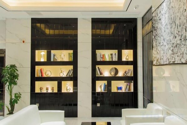 A lobby with two black shelving units displaying books and decorative items, a marble wall, and a potted plant. - Baise Changle Business Hotel (Baise)