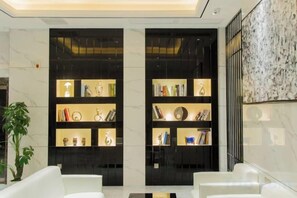 Un hall d’entrée avec deux étagères noires où sont exposés des livres et des objets décoratifs, un mur en marbre et une plante en pot.