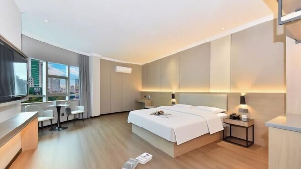 A modern hotel room with a bed, bedside tables, a desk, and a view of the city. - Baise Changle Business Hotel (Baise)