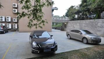Un área de estacionamiento con dos coches, un edificio con unidades de aire acondicionado y un árbol.