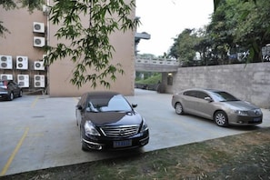A parking area with two cars, a building with air conditioning units, and a tree. - Baise Changle Business Hotel (Baise)