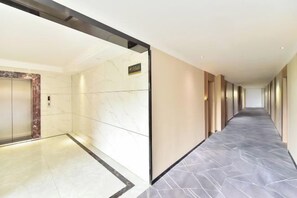 A long, narrow hallway with a marble floor, a wall-mounted elevator, and a door with a sign above it. - Baise Changle Business Hotel (Baise)