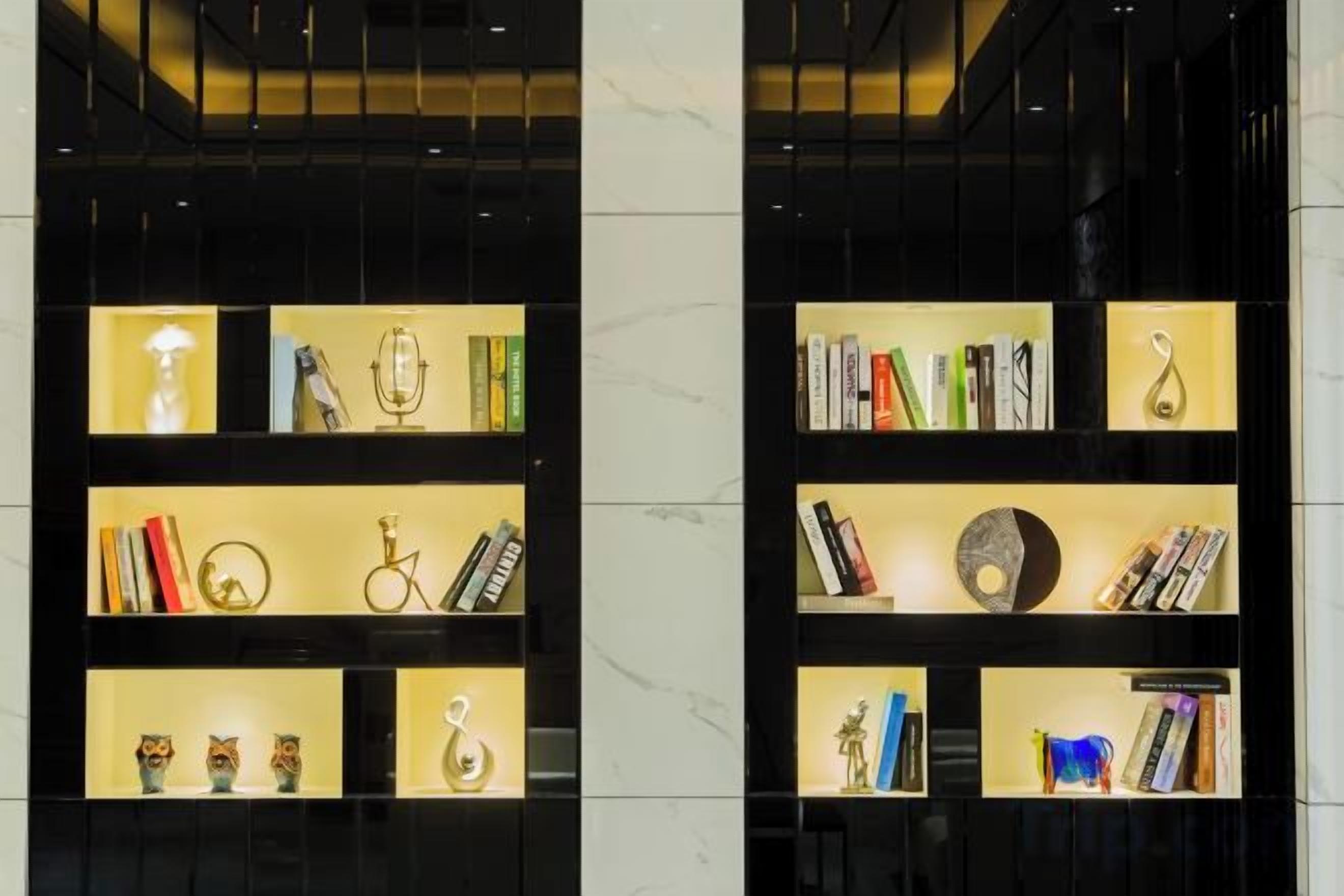 Dos estantes iluminados con libros, trofeos y objetos decorativos.