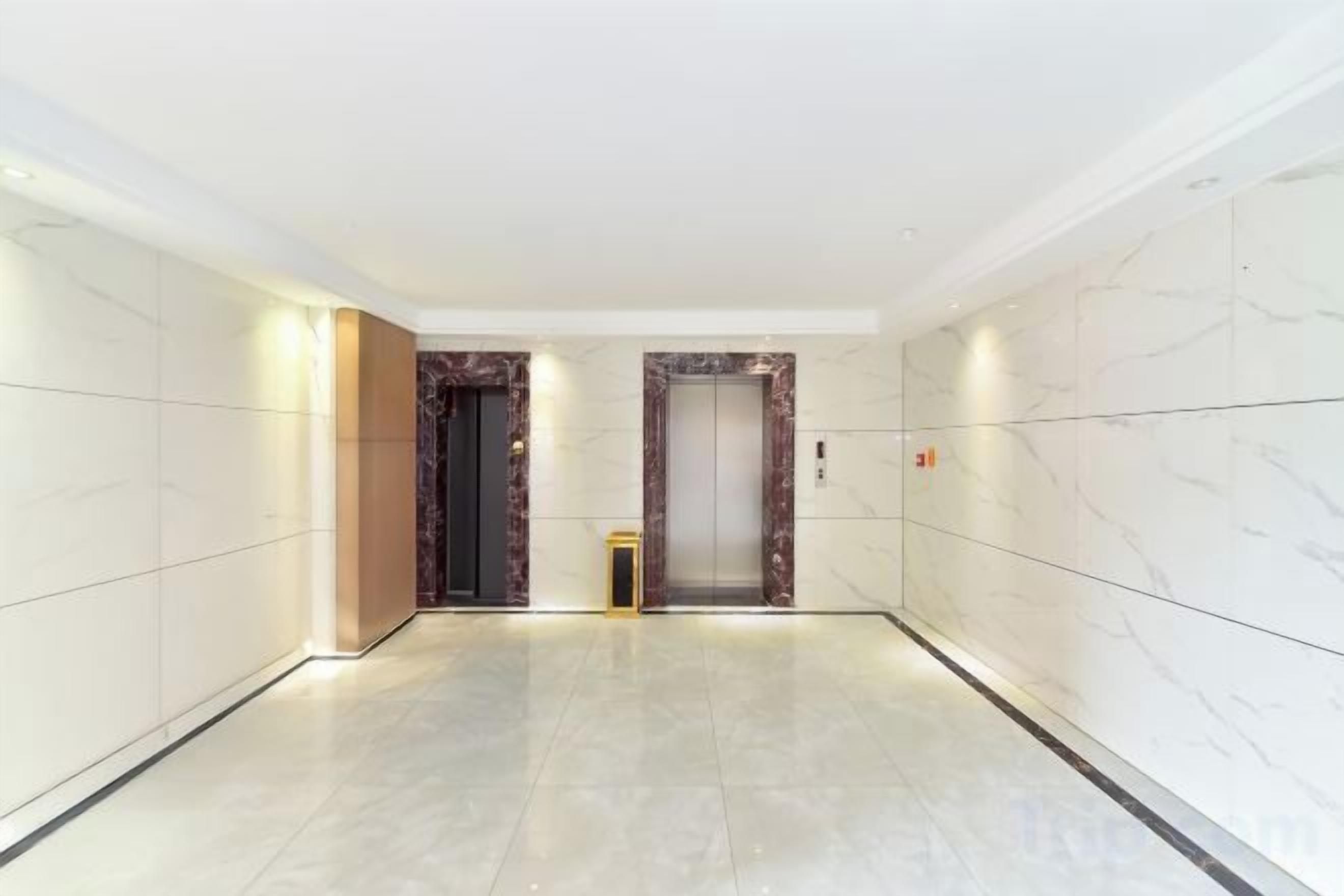 Un pasillo con dos ascensores, paredes de mármol y piso de baldosas.