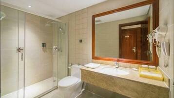 Un baño moderno con ducha de vidrio, inodoro y lavamanos con un espejo grande.