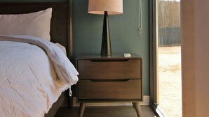 Un dormitorio con cama, mesita de noche, lámpara y un ventanal grande.