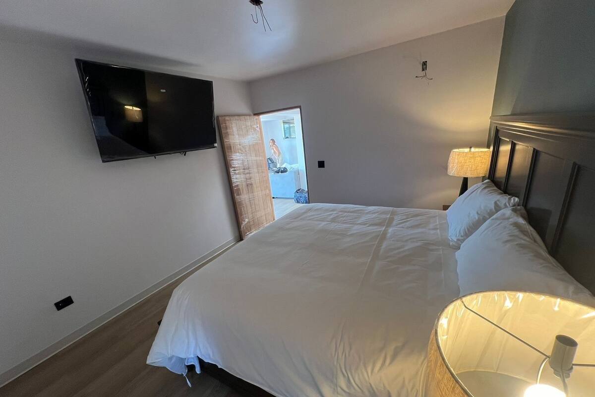 A bedroom with a bed, a TV mounted on the wall, and a lamp on the bedside table.