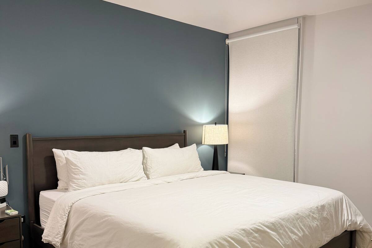A neatly made bed with white linens, a wooden headboard, and a bedside lamp.