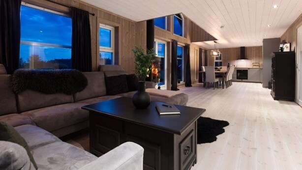 Una sala de estar moderna con un sofá, una mesa de centro y una chimenea. Se ve un área de cocina al fondo.