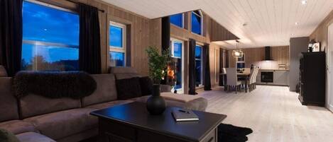 A modern living room with a sofa, a coffee table, and a fireplace. There is a kitchen area visible in the background.