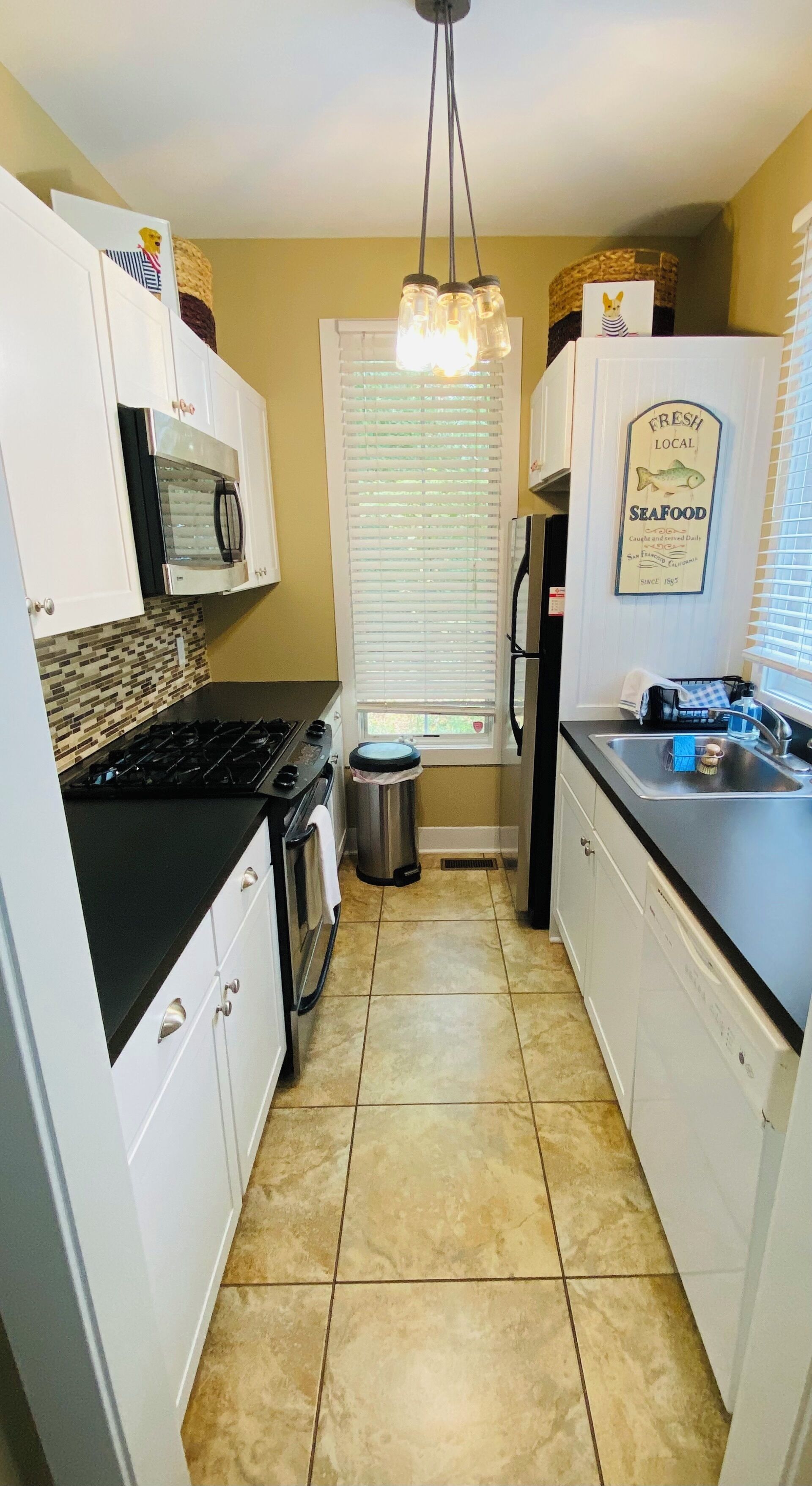 A compact kitchen with white cabinets, a black countertop, a stainless steel sink, and a tiled floor.