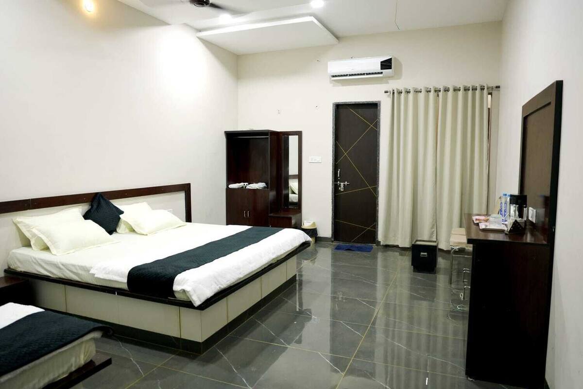 A hotel room with a bed, a wardrobe, a desk, and an air conditioning unit.