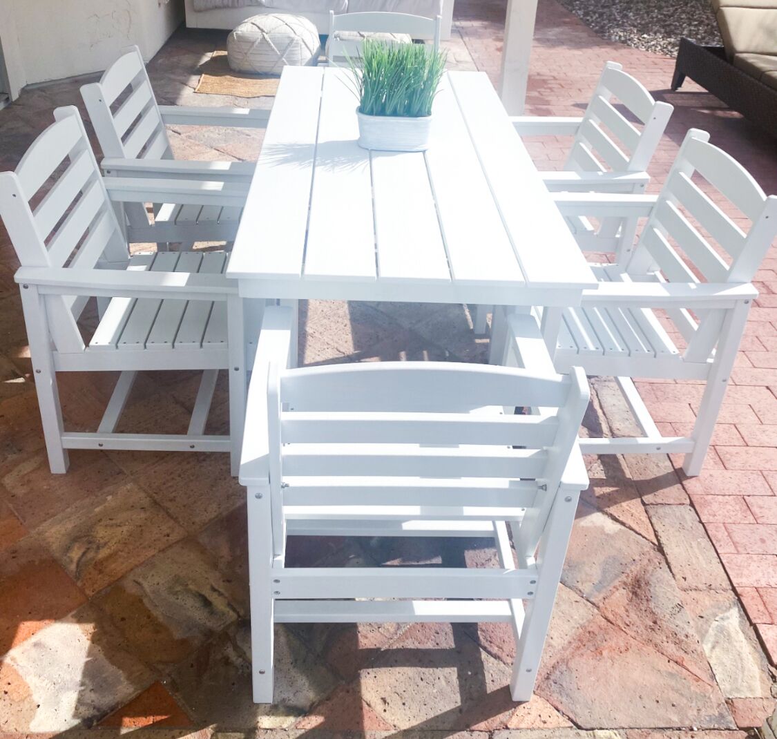A white wooden table with six matching chairs, a potted plant, and a stone-tiled floor.