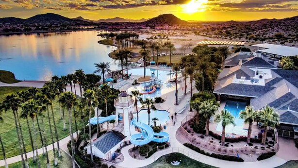 A resort with a large pool, water slides, and a view of the sunset over a body of water.