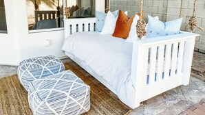 A white bed with a swing, two geometric ottomans, and a view of a brick wall and greenery outside.