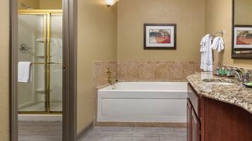 A bathroom with a bathtub, a shower, a sink with toiletries, and a framed picture on the wall.