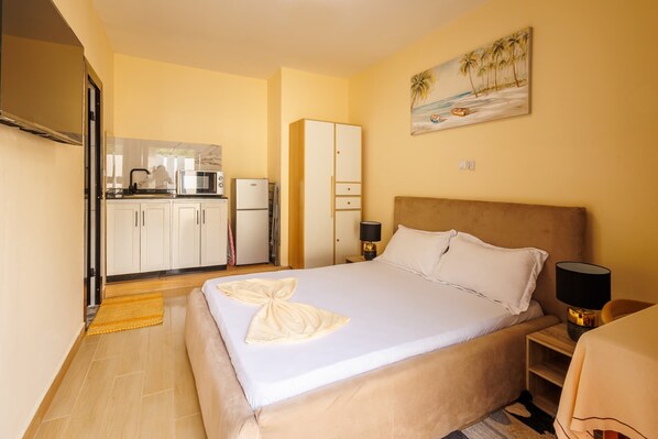 A hotel room with a bed, bedside table, lamp, and a painting of a beach scene.