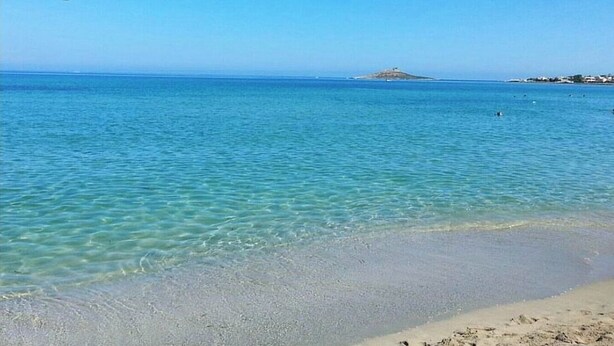 A beach with clear blue water, a sandy shore, and a distant island.