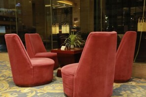A lobby with four red chairs, a small table with a plant, and a patterned carpet. - Ruijin Hotel (Dabu)