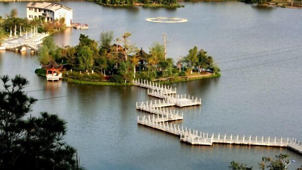 Una propiedad frente al lago con un muelle que se adentra en el agua, rodeada de vegetación y un pequeño edificio.