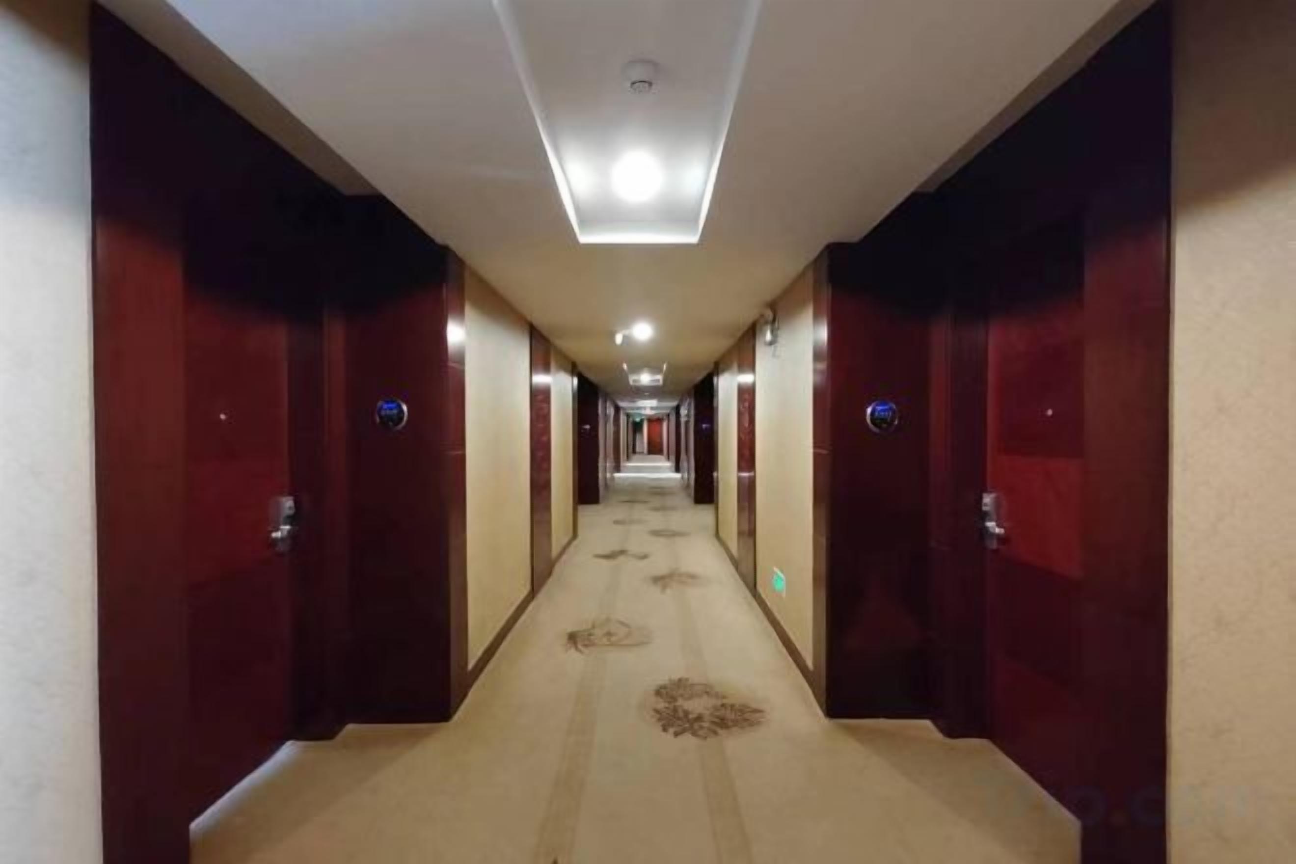 Un couloir d’hôtel avec des portes des deux côtés, un sol recouvert de moquette et un luminaire au plafond.