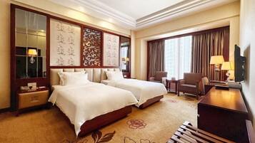 A hotel room with two beds, a desk, a chair, a TV, and a large window with curtains.