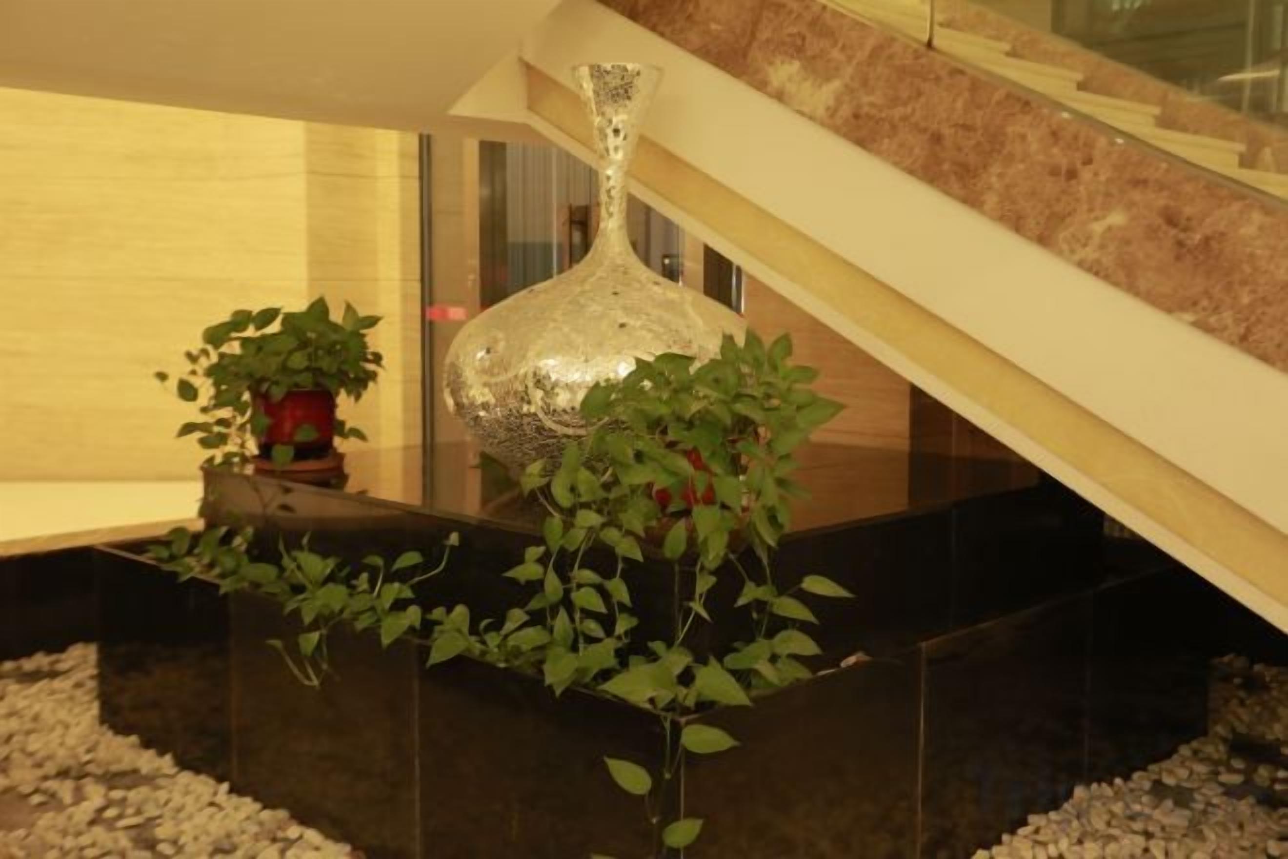 A modern interior with a staircase, a large decorative vase, and potted plants.