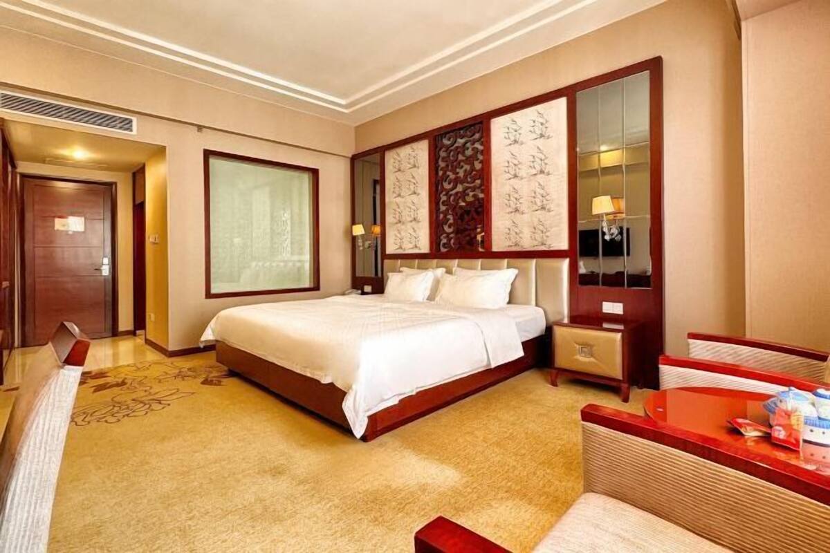 A hotel room with a large bed, a desk, a chair, a mirror, and a television.