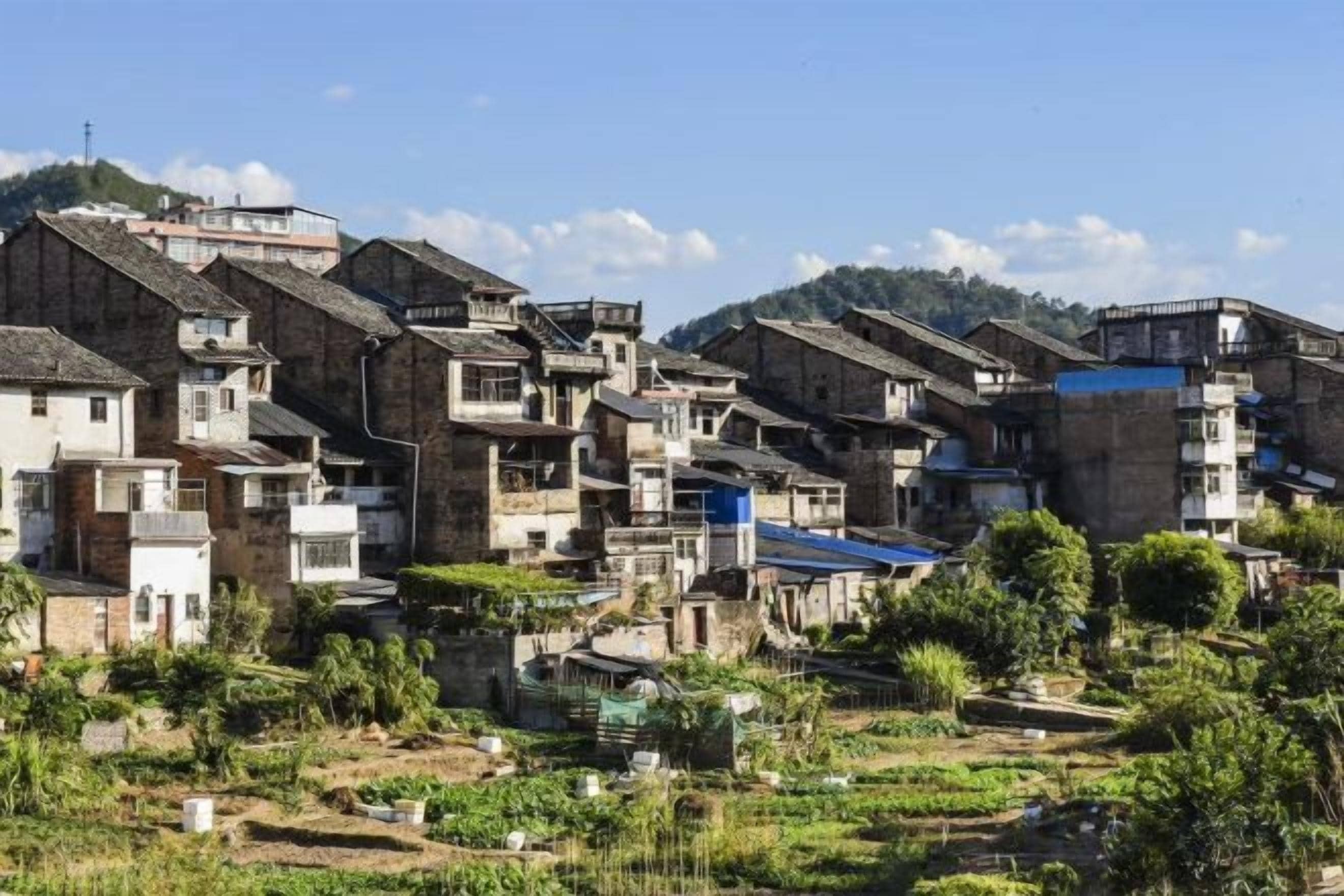 Un village traditionnel avec des bâtiments à étages, des jardins en terrasses et un paysage montagneux en arrière-plan.