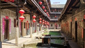 Un patio tradicional con edificios de ladrillo, faroles rojos y una pequeña fuente.