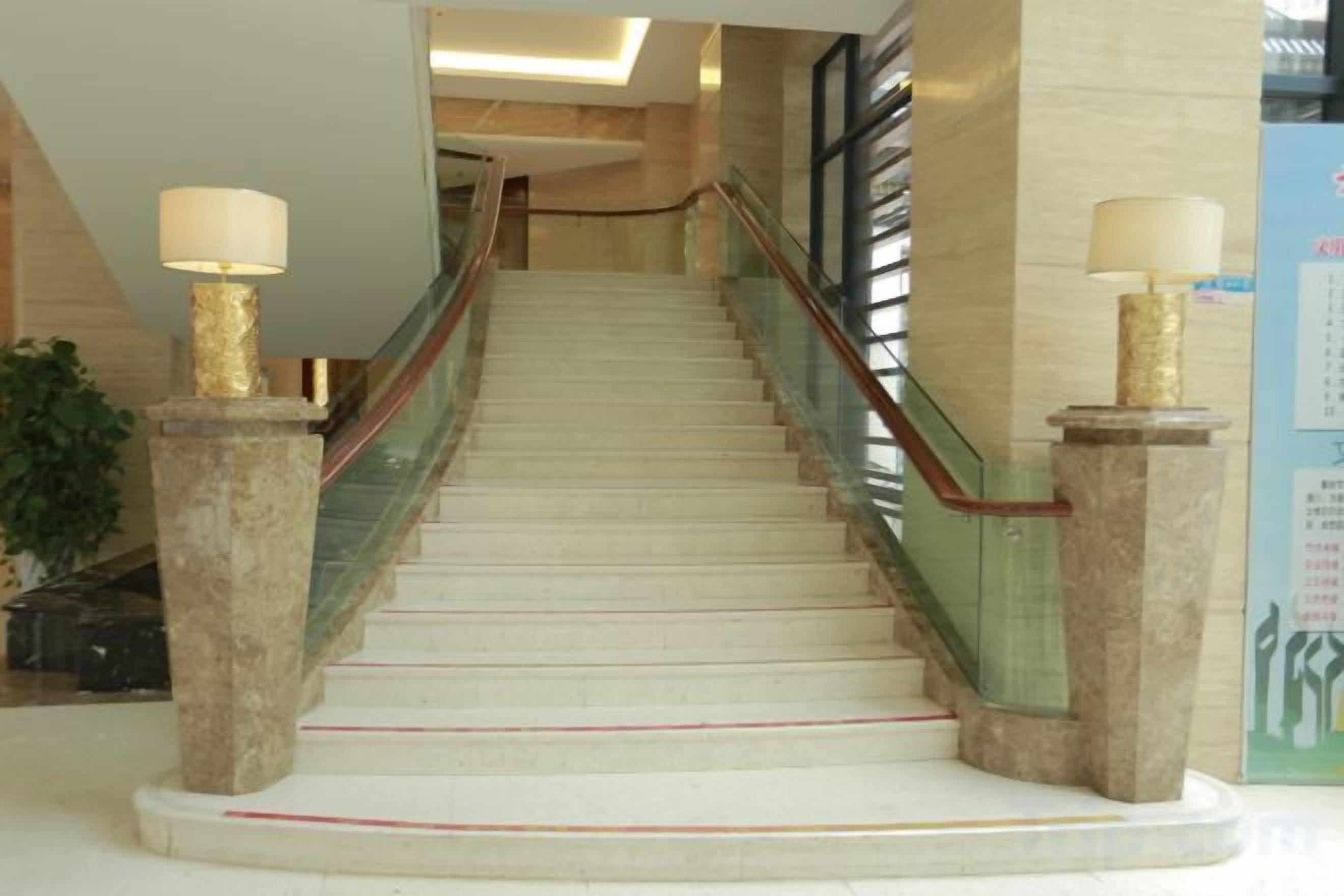 Una escalera de mármol con barandillas de vidrio y dos lámparas a cada lado.