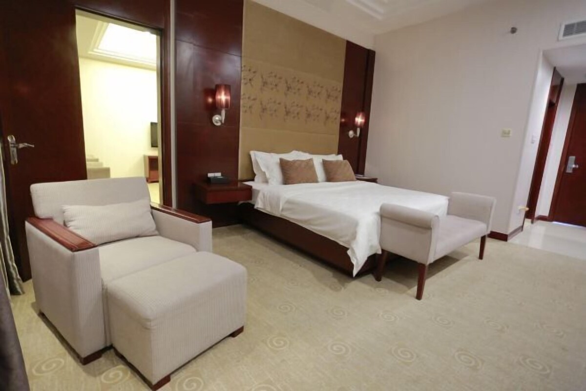 A hotel room with a bed, two armchairs, a nightstand, and a wall-mounted light fixture.