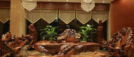 A lobby with a central wooden sculpture, chandeliers, and patterned curtains.