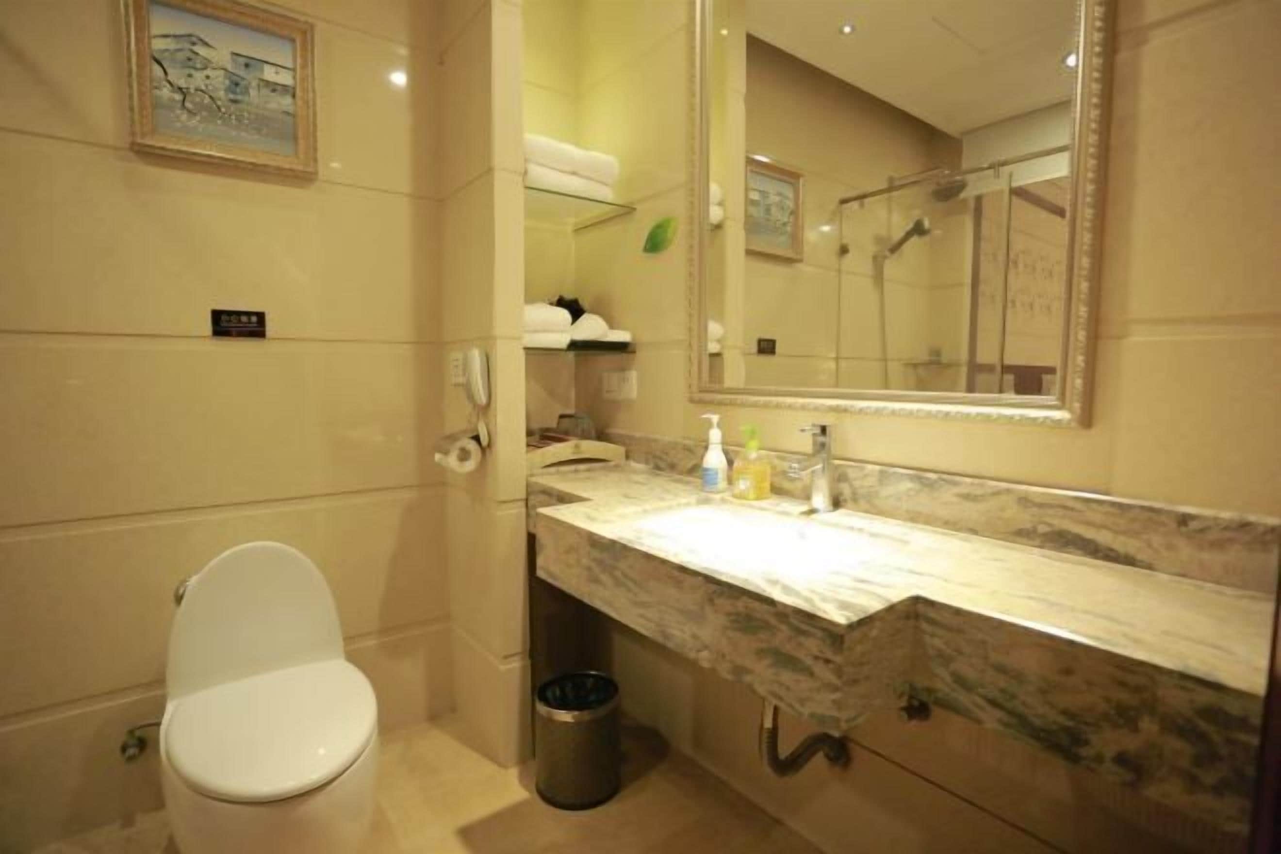 A bathroom with a toilet, a sink with a marble countertop, a mirror, and a trash can.