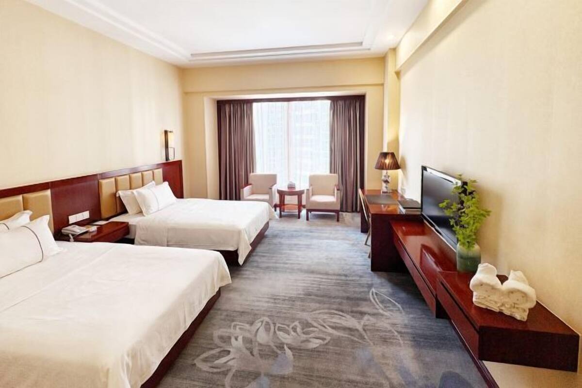 A hotel room with two beds, a TV, a desk, and a chair.