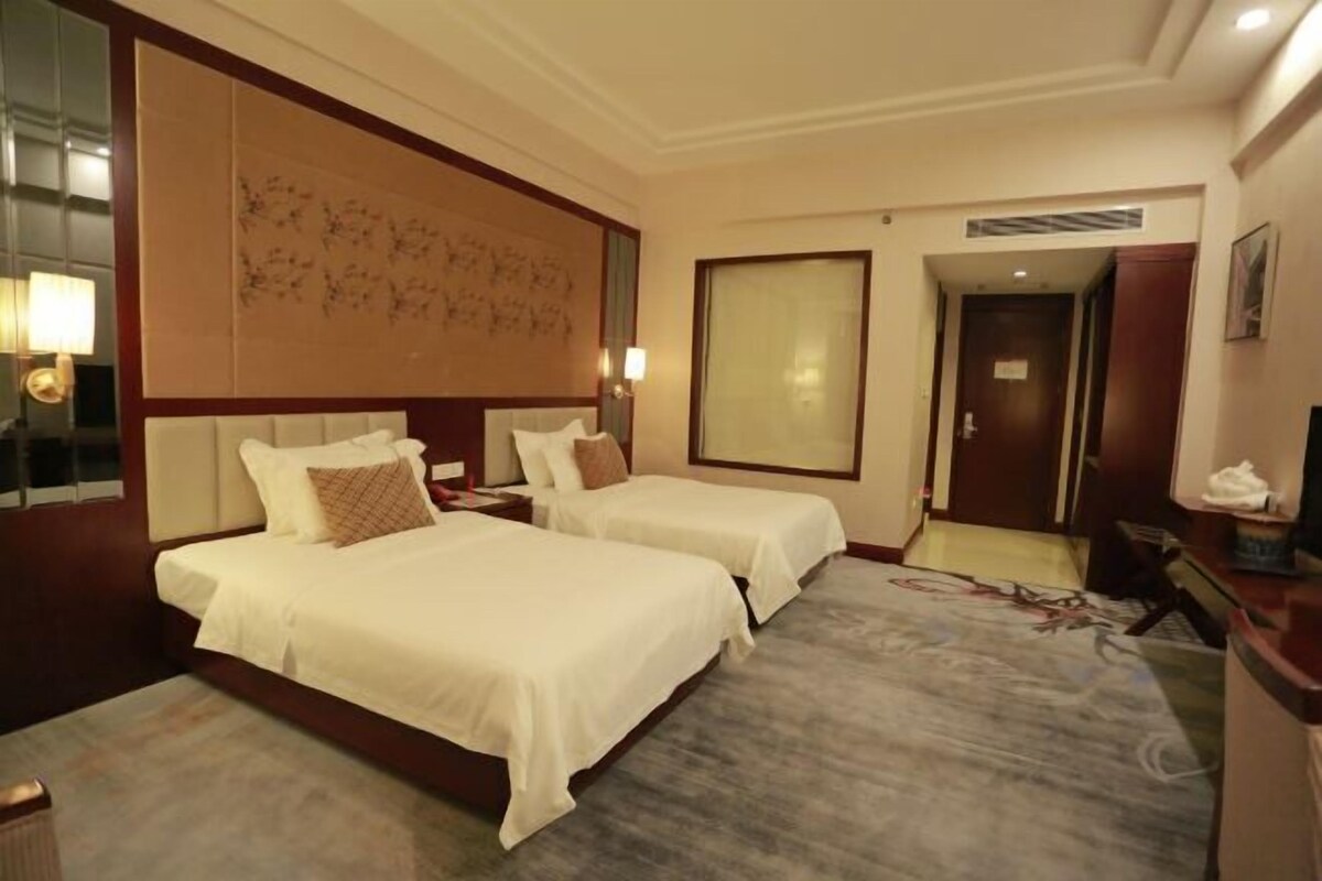 A hotel room with two beds, a large mirror, a wall art piece, and a carpeted floor.