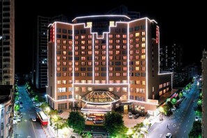 A multi-story hotel with a central atrium, surrounded by a parking area and a street with vehicles. - Ruijin Hotel (Dabu)