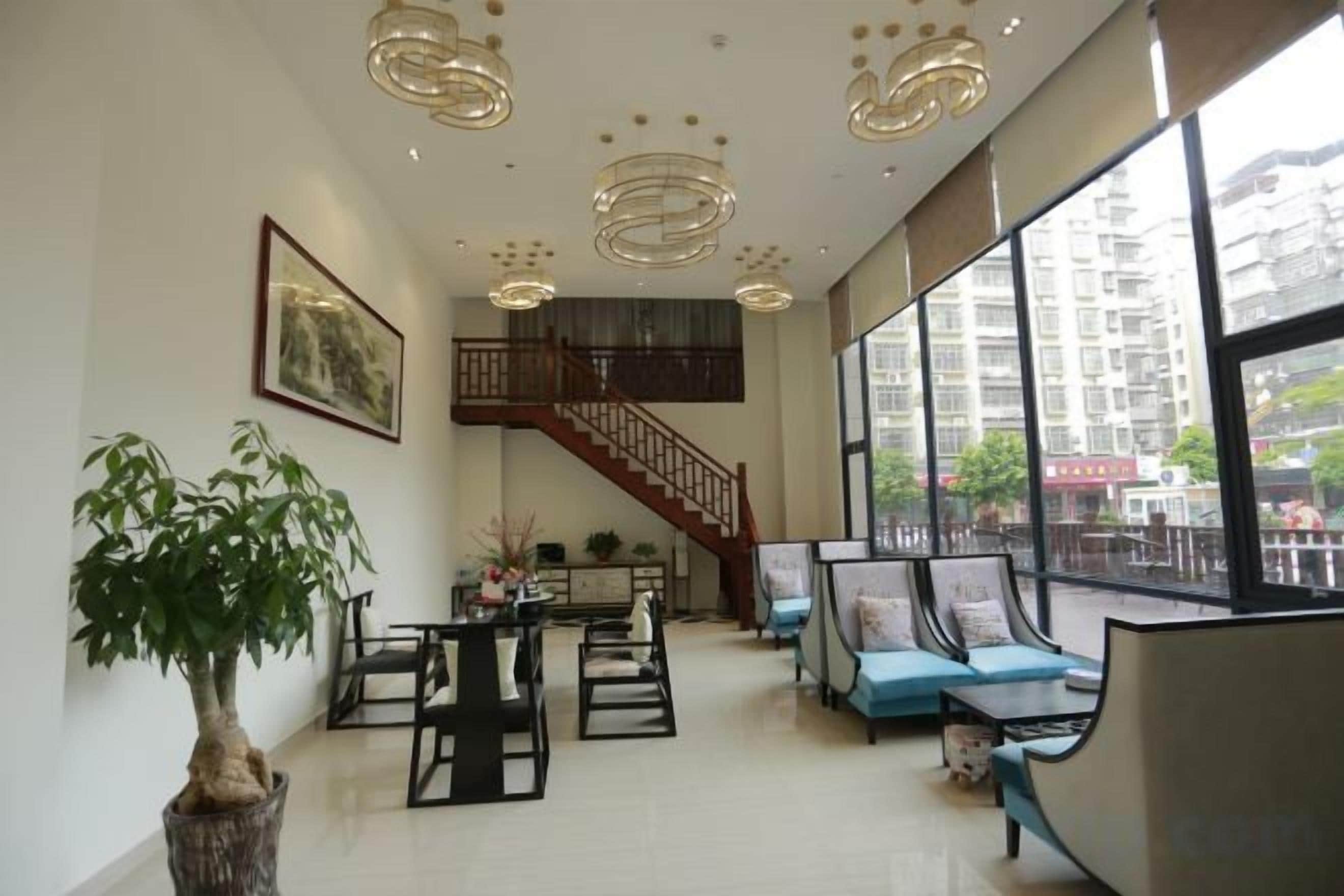 A spacious living area with a staircase, seating arrangements, and large windows.