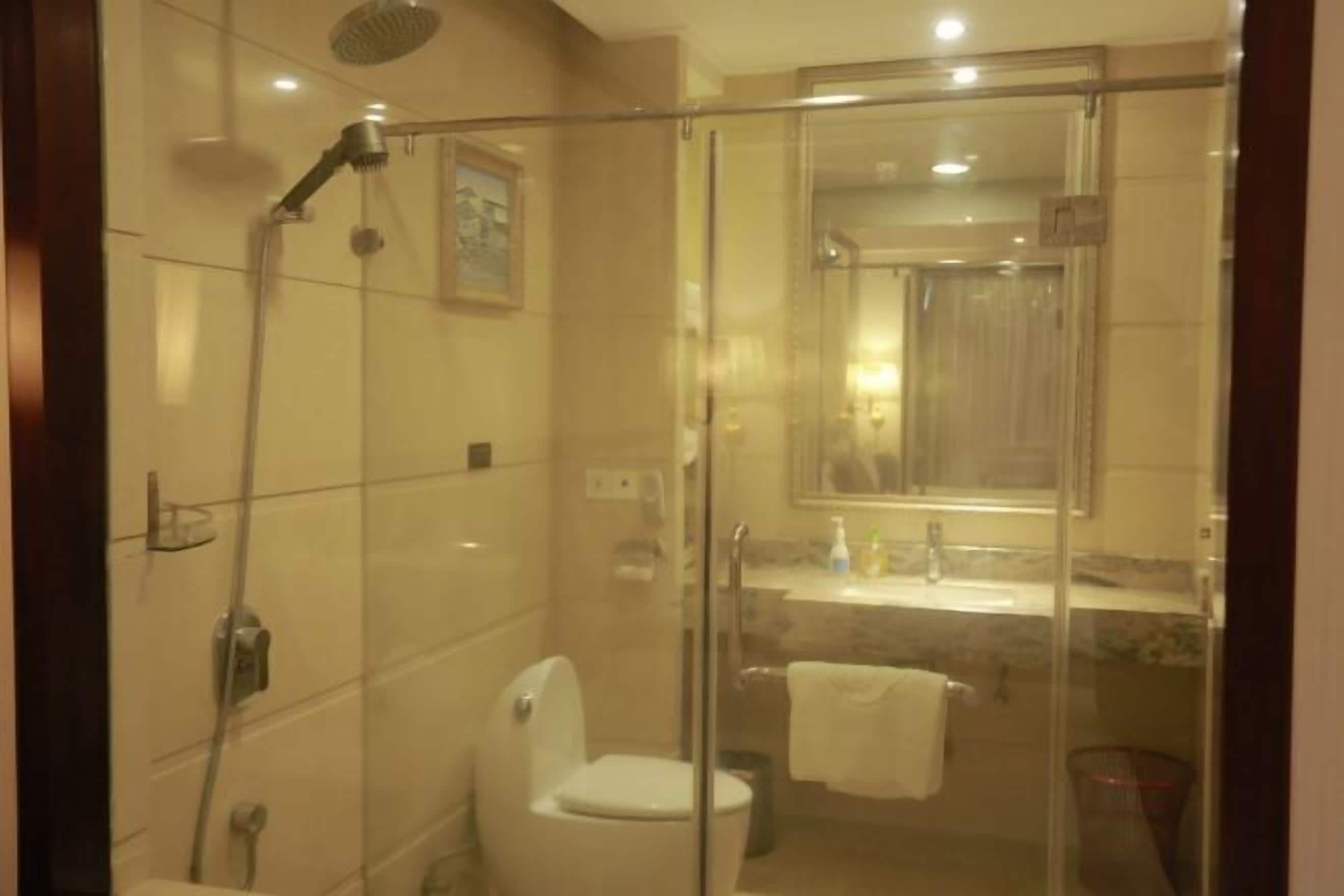 Egy modern fürőszoba üvegfalas zuhanyzóval, WC-vel és egy mosdókagylóval, mely felett tükör található.