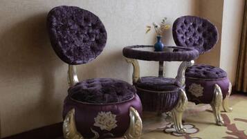 A room with two purple upholstered chairs with gold accents and a small round table with a vase.